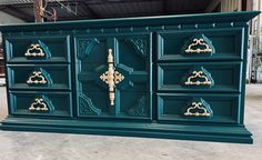 a green dresser with gold handles and ornate carvings on the doors is in a warehouse