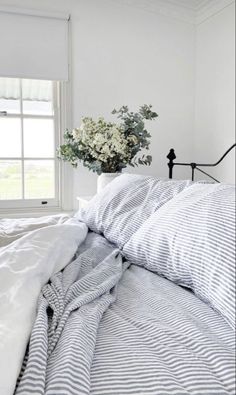 a bed with blue and white striped comforter in front of a window next to a plant