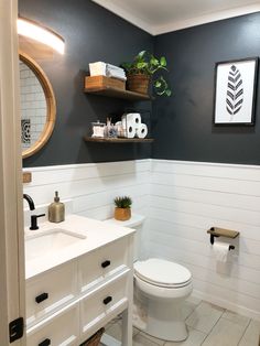 a white toilet sitting in a bathroom next to a sink and wooden shelves above it