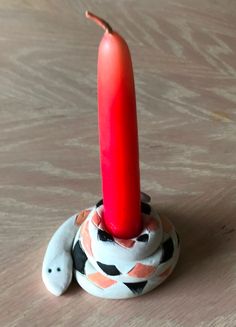 a red candle sitting on top of a white elephant figurine with a black and orange design