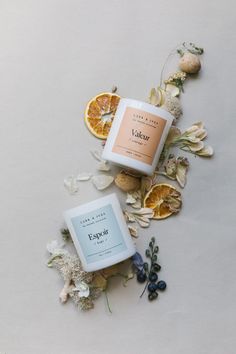 two oranges and some flowers on a white surface with an empty jar next to it