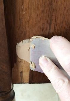 a hand is holding a piece of wood in front of a door with peeling paint on it