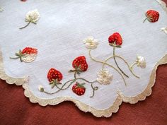 a white doily with strawberries and flowers on it, sitting on a red surface