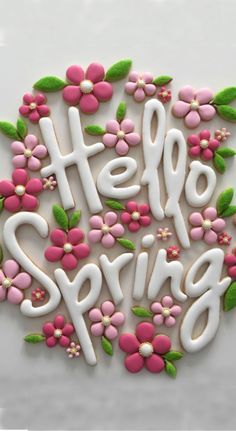 a cookie with the words hello spring written in white frosting and decorated with pink flowers