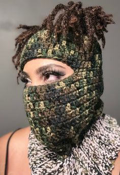 a woman with dreadlocks wearing a green and brown knitted scarf over her face