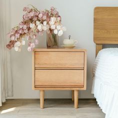 a nightstand with flowers and a cup on it next to a bed in a bedroom