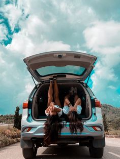 two women are laying down in the back of a car with their feet on the trunk