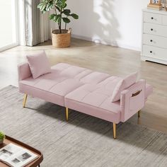 a pink couch sitting on top of a wooden floor next to a white dresser and potted plant