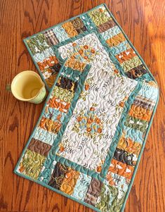 a wooden table with a quilted placemat and cup on it, next to a yellow mug