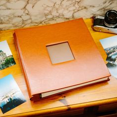 an open book sitting on top of a wooden table next to pictures and a camera