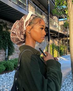 a woman standing next to a tree with an umbrella over her head and holding a cell phone in her hand