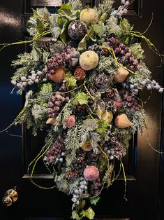 a wreath is hanging on the door with pine cones, berries and other decorations around it