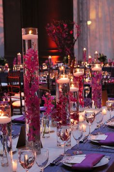 the table is set with candles, plates and flowers in tall vases on each side