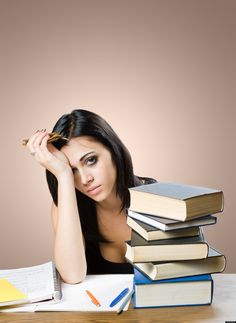 a woman sitting at a table with books and pens in front of her, holding her head