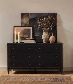 two vases on top of a black dresser with candles and pictures above the drawers