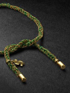 a green and gold colored cord with two golden bells on it, sitting on a black surface