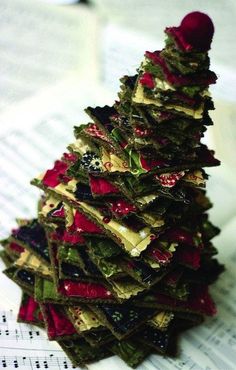 a small christmas tree made out of old clothes on top of sheet music paper with red pom - pom