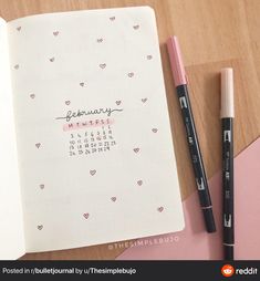 an open notebook with a calendar and two markers on it next to a pink pen