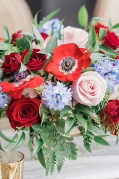 a vase filled with red, white and blue flowers on top of a table next to a gold cup