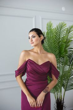 a woman in a long purple dress standing next to a potted plant and looking off into the distance