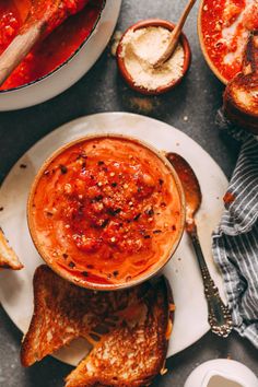 a bowl of soup on a plate with bread and spoons next to the bowl