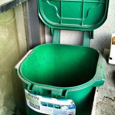 a green trash can sitting next to a wall