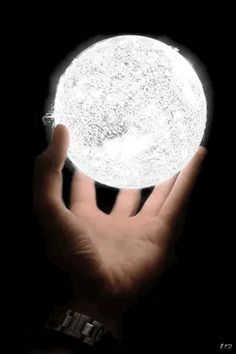 a person's hand holding a glowing white ball in the dark with their fingers