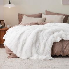 a bed covered in white fluffy blankets and pillows next to a night stand with a lamp on it