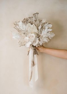 a bridal bouquet being held by someone's hand on a beige wall background