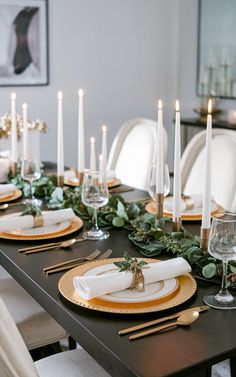 a table set with place settings, candles and greenery on the plates in front of it