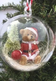 a glass ornament with a teddy bear in a santa suit sitting on top of a tree