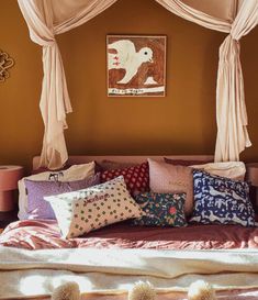 a bed with lots of pillows on top of it next to a painting and curtains