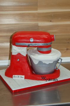 a red and white cake mixer sitting on top of a metal counter next to a wooden wall