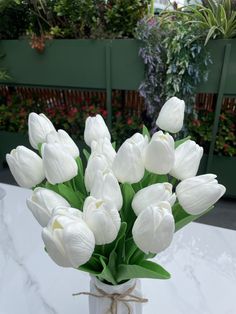 a vase filled with white flowers on top of a marble table covered in greenery