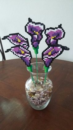 three purple flowers in a vase filled with rocks