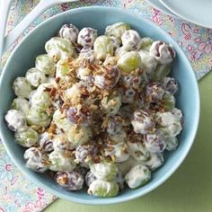 a blue bowl filled with salad next to a white plate and spoon on top of a table