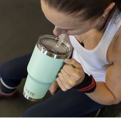 a woman drinking from a cup while sitting on the floor