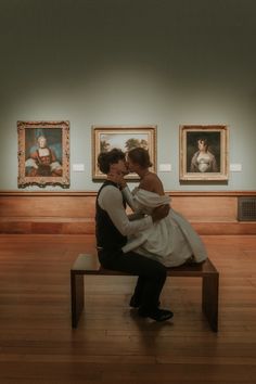 a man and woman sitting on a bench in an art gallery with paintings behind them