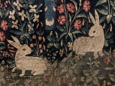 two white rabbits sitting in the grass near flowers and butterflies on a tapestry wall hanging