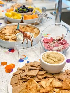 a table topped with bowls filled with different types of snacks and dips on top of plates