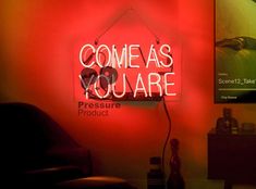 a neon sign that says come as you are on the wall next to a chair