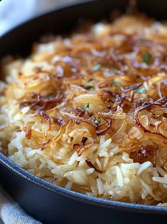 a pan filled with rice and onions on top of a wooden table next to a white towel