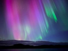 an aurora bore is seen in the night sky over water and mountains with bright lights