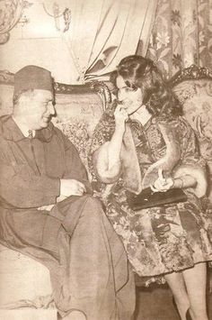 an old black and white photo of a man and woman sitting on a couch talking to each other