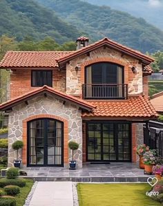 a house that is in the middle of some bushes and trees with mountains in the background