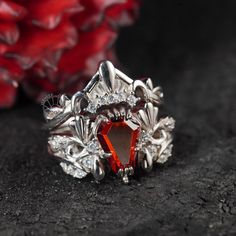 a ring with an orange stone surrounded by white diamonds on a black surface next to red flowers