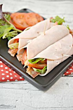 two wraps are on a black plate with tomatoes and lettuce in the background