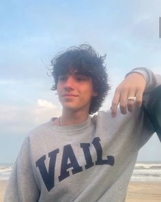 a young man standing on top of a beach next to the ocean with his hand on his hip