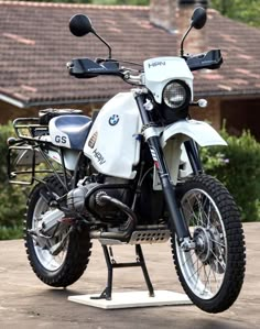 a white and black motorcycle parked on top of a parking lot next to a house