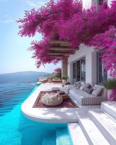 an outdoor living area with purple flowers on the trees and water in the pool below